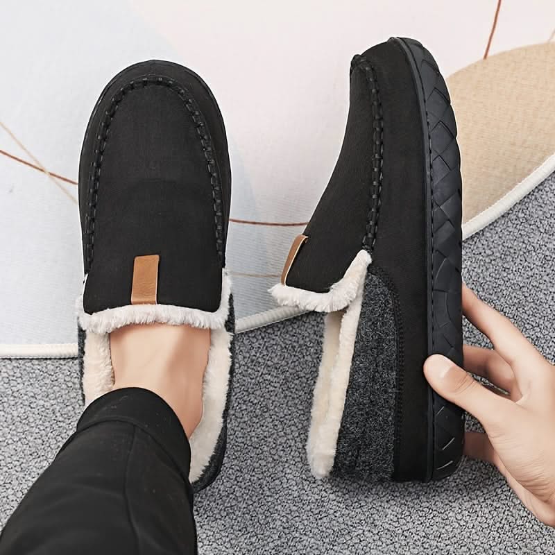 Black slippers with white fur lining worn by a person on a textured floor.