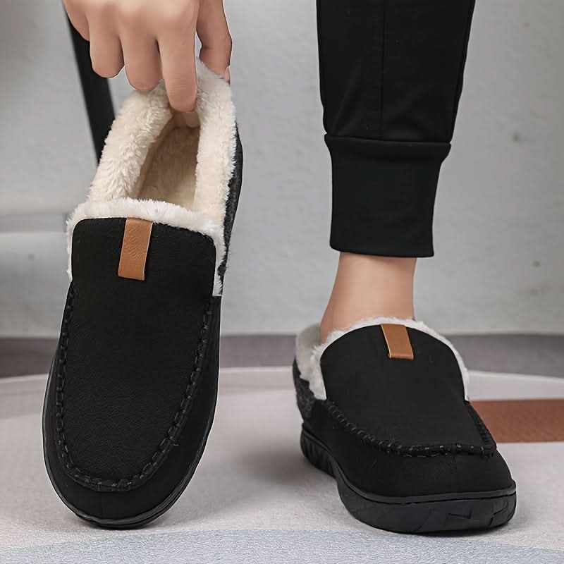 Black slip-on shoes with white fur lining worn by a person on a neutral background