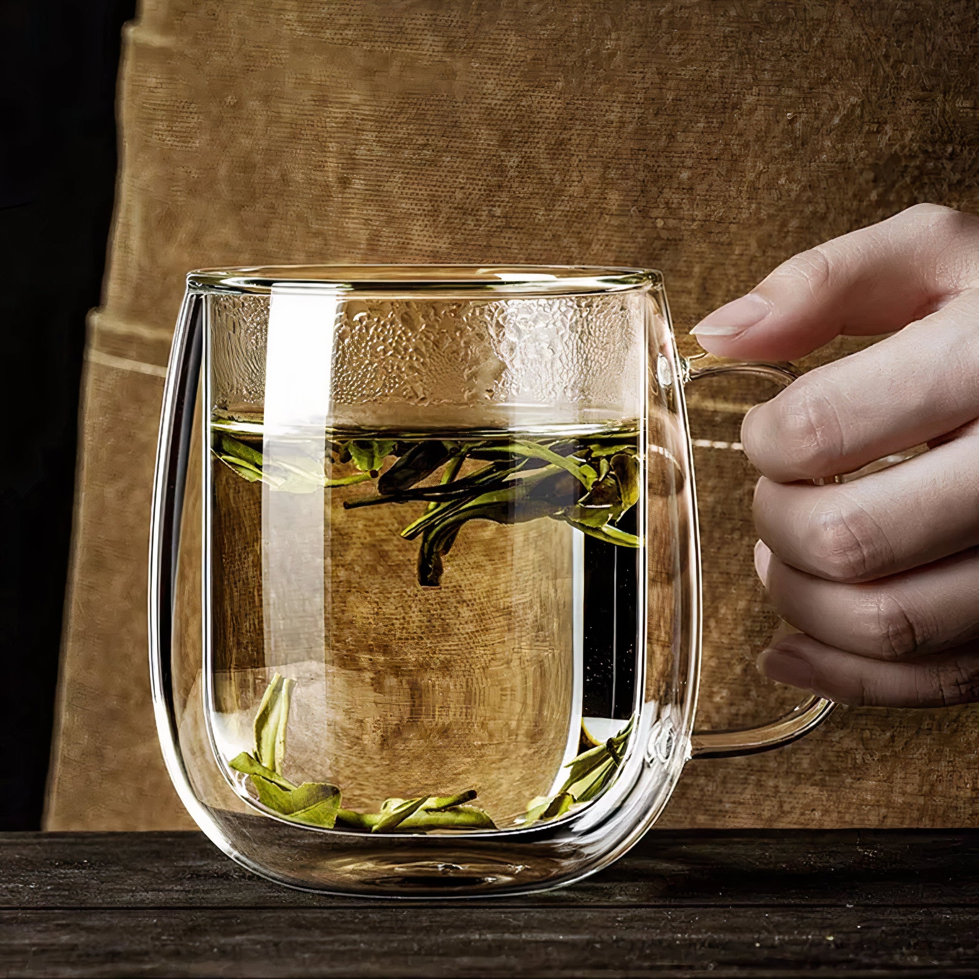 Clear glass mug with tea leaves held by a hand against a wooden background
