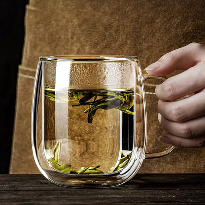 Clear glass mug with tea leaves held by a hand against a wooden background