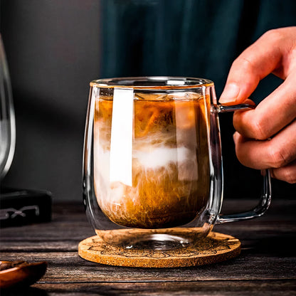 Glass mug with layered drink on a wooden coaster, held by a hand.