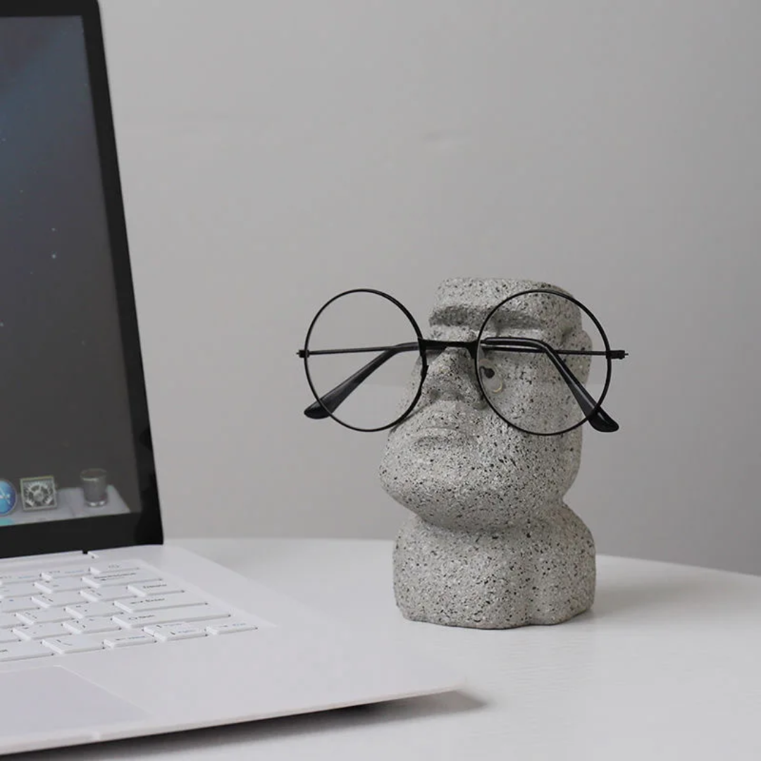 Concrete sculpture of a face wearing glasses on a desk with a laptop in the background