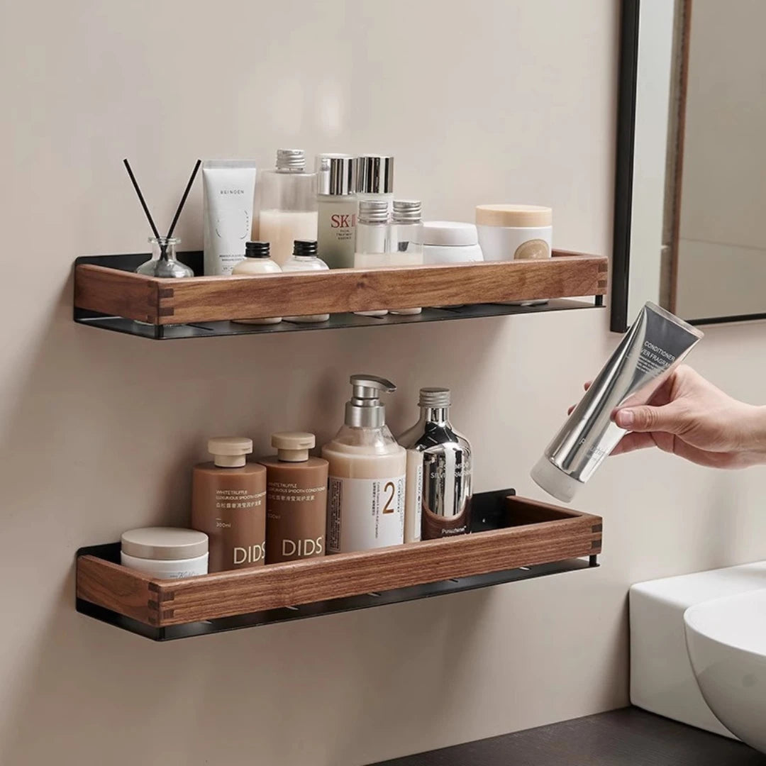 Josh & Tate - TimberLedge™ Wall Organizer - Two floating wooden bathroom shelves with black metal brackets, styled with toiletries and a hand holding a silver tube, against a beige wall.