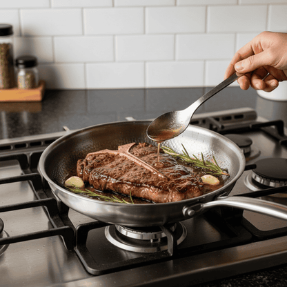 Person cooking steak in a pan on a stove with a spoon
