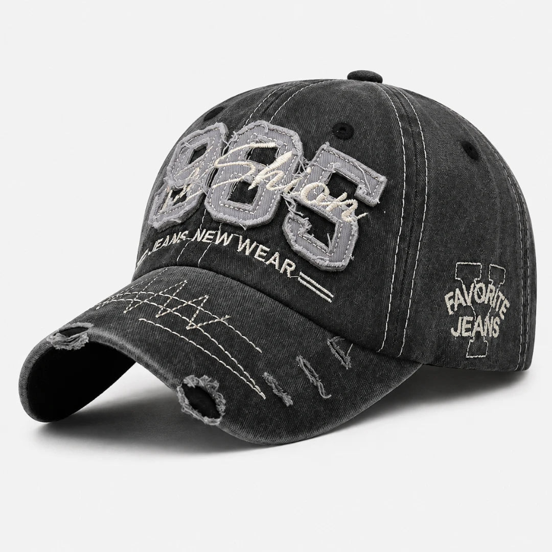 Josh & Tate - TrailFade™ '85 Cap - A distressed black washed baseball cap with embroidered details. The front features large gray and white embroidered '985' and 'Fashion' text, with 'FASHIONS NEW WEAR' underneath.