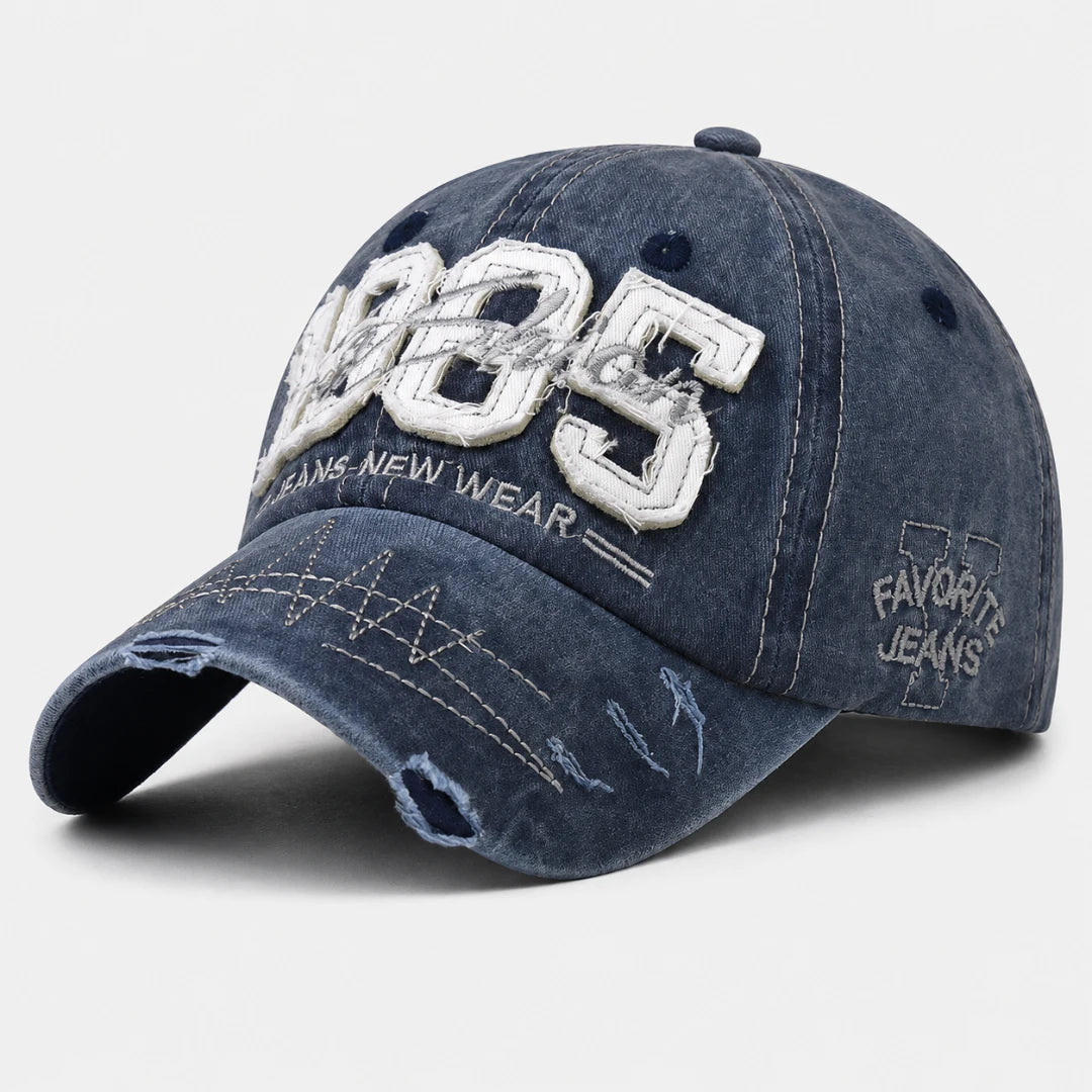 Josh & Tate - TrailFade™ '85 Cap - A distressed dark blue denim baseball cap with white embroidered lettering on the front and side, shown on a light gray background.