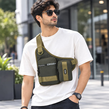 Josh & Tate - UrbanCore™ Crossbody Bag - A man wearing a white t-shirt and sunglasses models an olive green sling-style crossbody phone bag with multiple zippered pockets on a modern outdoor walkway.