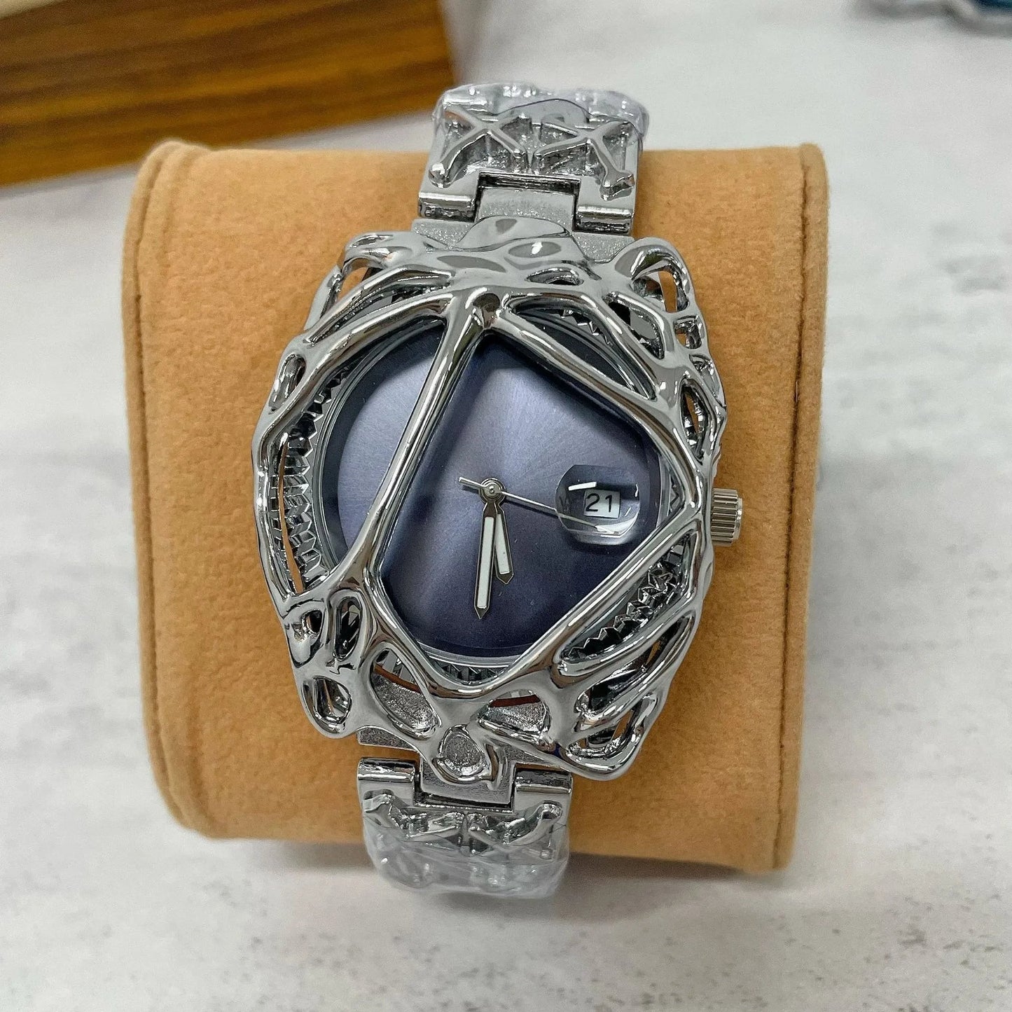 Silver wristwatch with intricate design on a beige cushion