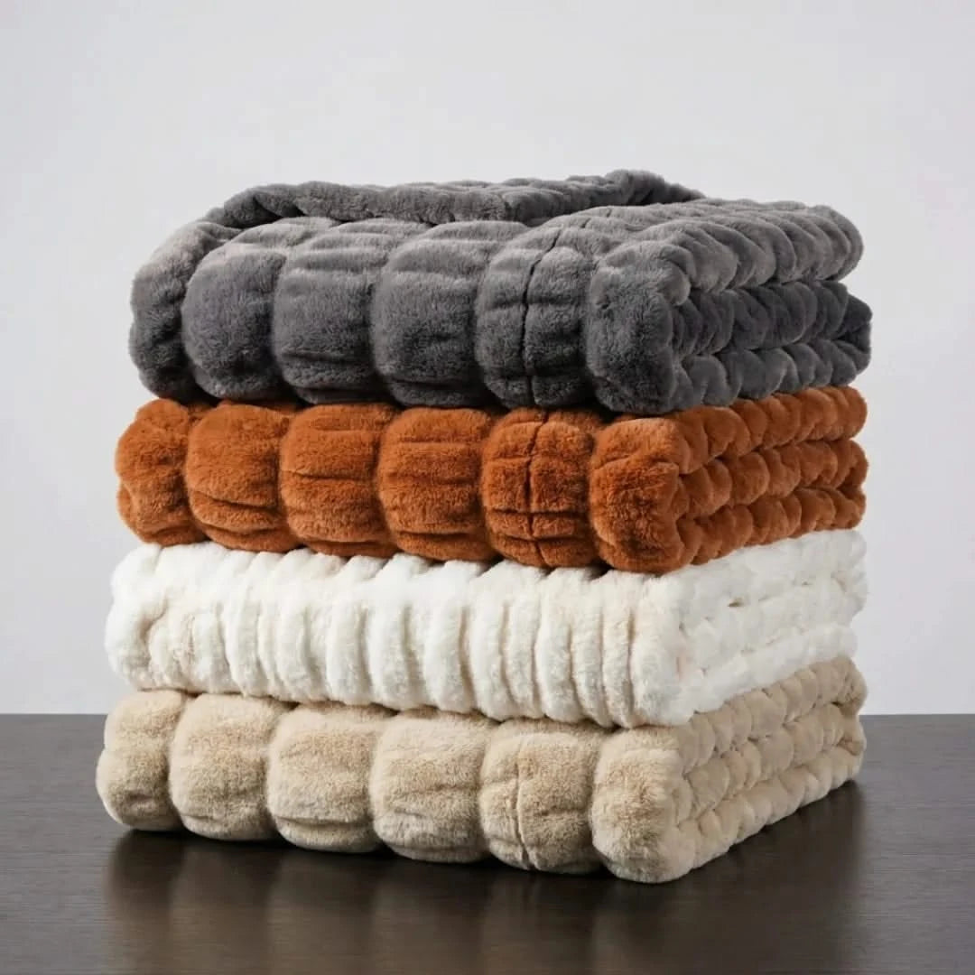Josh & Tate - VelvetRib™ Faux Fur Throw Blanket - Stack of textured blankets in gray, brown, white, and beige on a dark surface with a light gray background.
