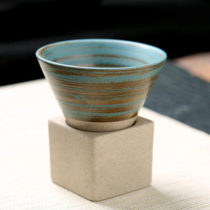 Ceramic cup with blue and brown glaze on a beige stand against a blurred background