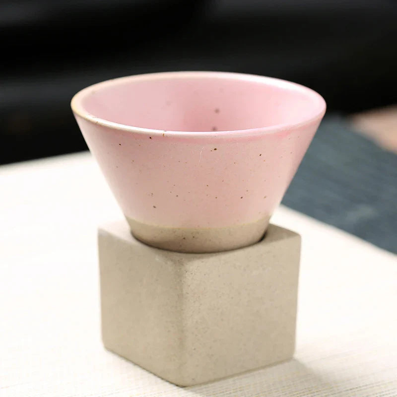 Pink ceramic cup on a beige cube with a blurred background