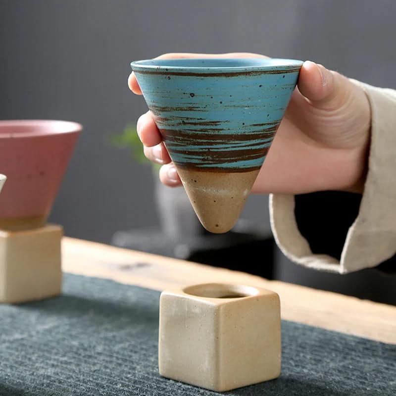 Hand holding a blue ceramic cup with a brown base on a dark surface