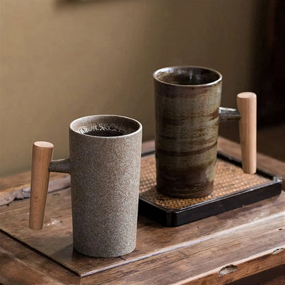 Two ceramic cups with wooden handles on a wooden surface.