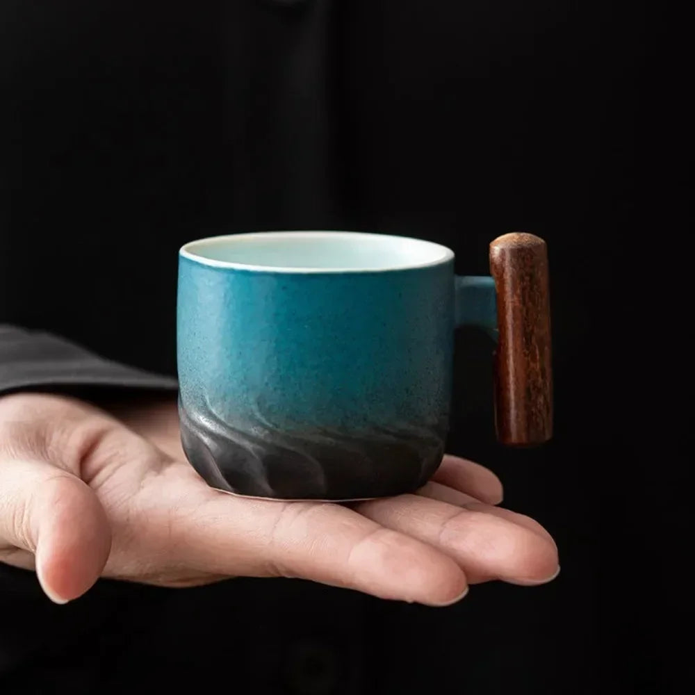 Blue ceramic mug with a wooden handle held in a hand against a black background