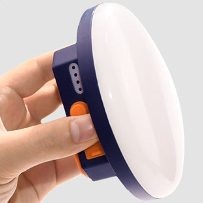 Hand holding a round, blue and white device with an orange button on a light gray background