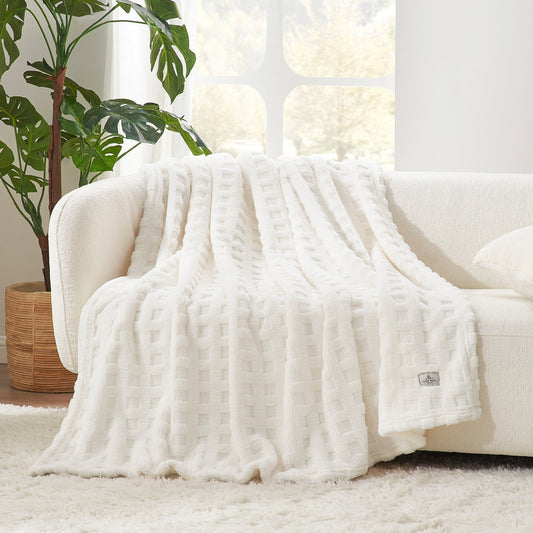 White textured blanket draped over a white sofa in a bright living room with plants.