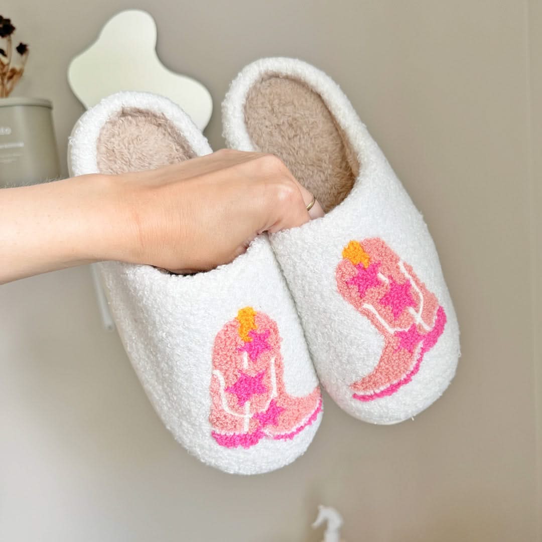 White slippers with pink and orange designs held by a hand against a neutral background