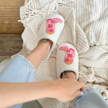 White slippers with pink and orange designs worn by a person on a textured surface.