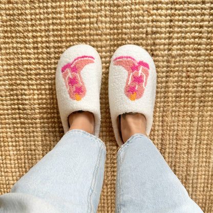 White slippers with pink and orange designs on a textured beige carpet