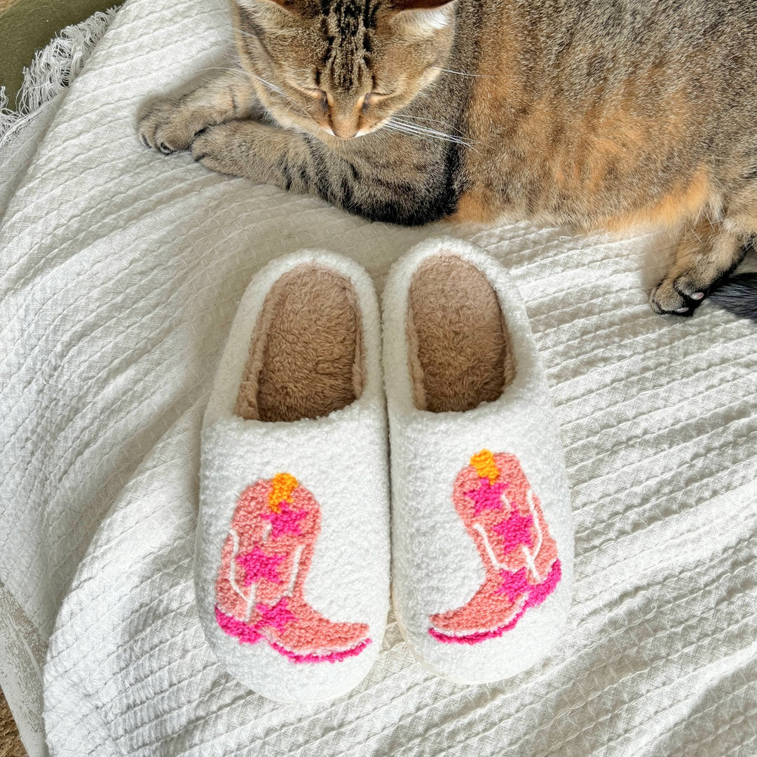 Cat lying on a blanket with a pair of white socks featuring pink cowboy boot designs.