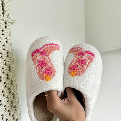 White slippers with pink and orange design held by a hand against a white background