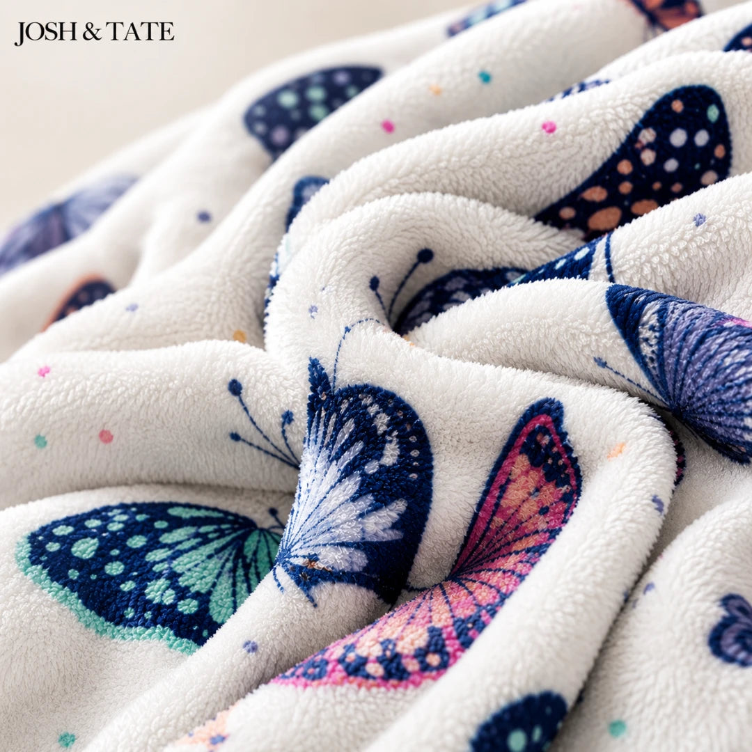 Josh & Tate - WingWrap™ Butterfly Throw Blanket - Close-up of fabric with colorful butterfly patterns, featuring the brand 'JOSH & TATE'.