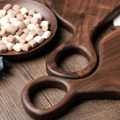 Wooden serving board with handles on a wooden surface, next to a bowl of marshmallows.