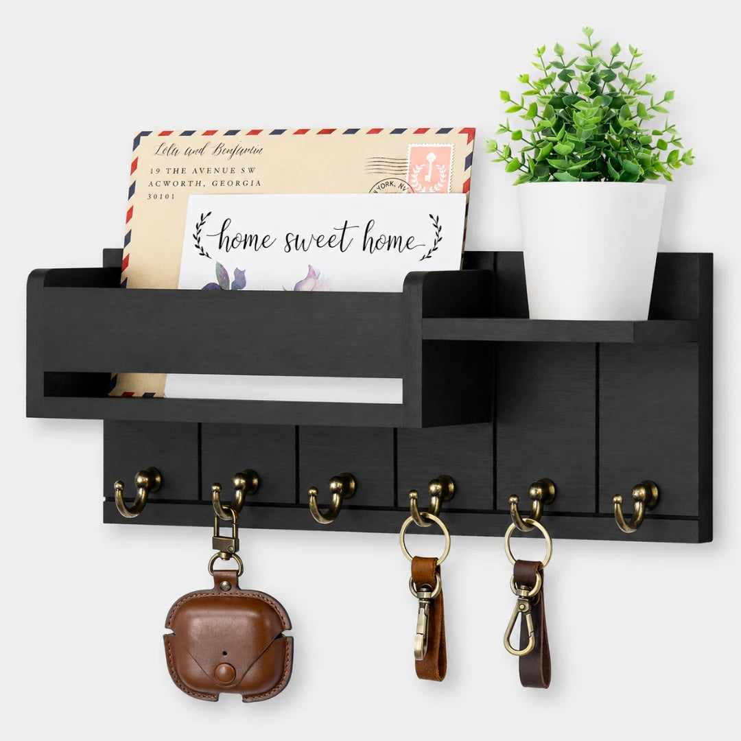 Josh & Tate - WoodenRack™ Wall Organizer - Black wall-mounted storage shelf with five brass hooks, a mail slot, an envelope holder, and a plant pot, shown against a white wall with decorative props.
