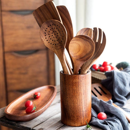 Set of wooden kitchen utensils in a wooden holder on a rustic wooden surface.