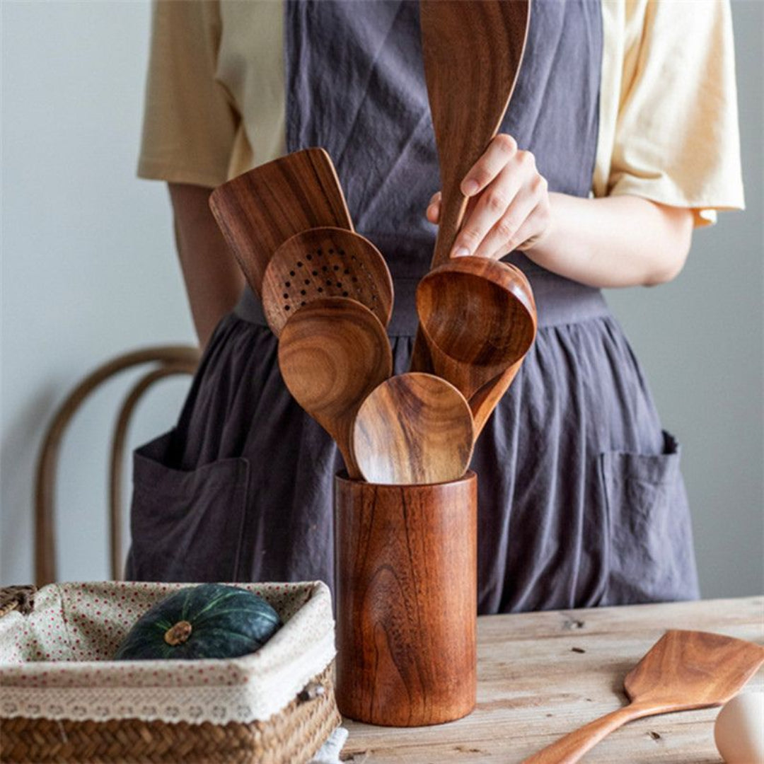 Person holding wooden utensils in a wooden container on a table.