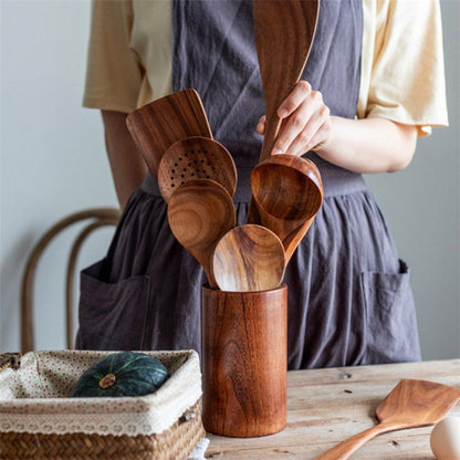 Person holding wooden utensils in a wooden container on a table.