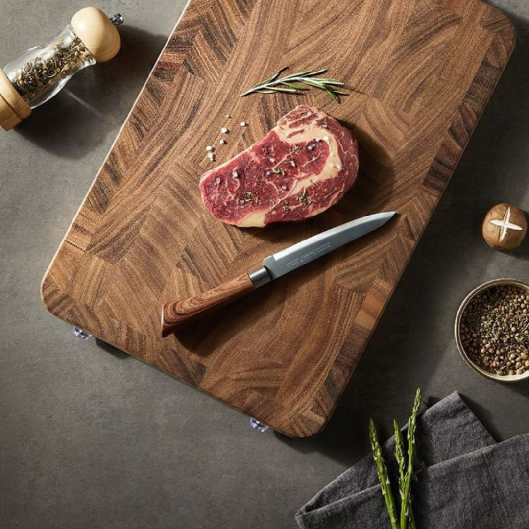 Raw steak on a wooden cutting board with a knife, pepper grinder, and seasonings.