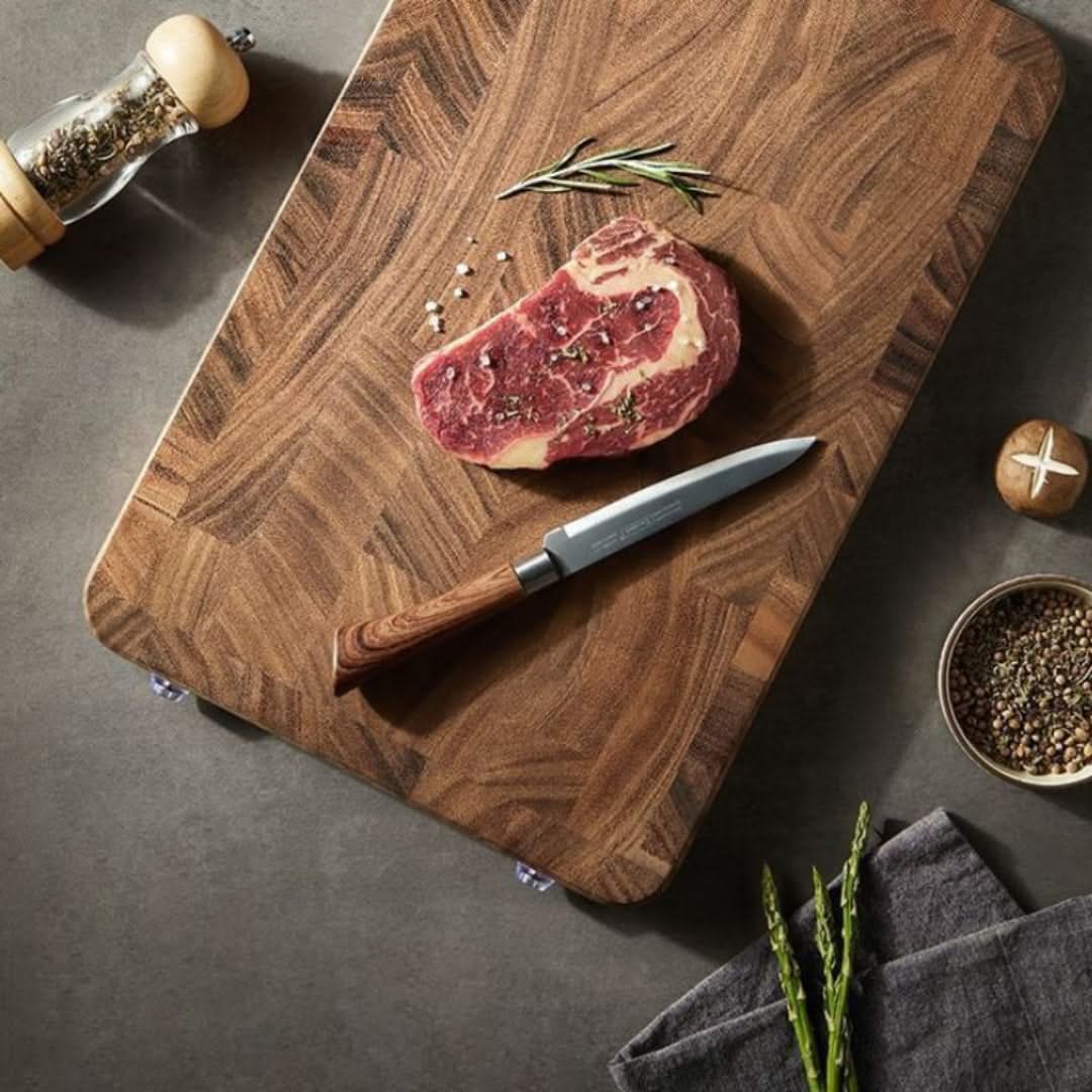 Raw steak on a wooden cutting board with a knife, pepper grinder, and seasonings.