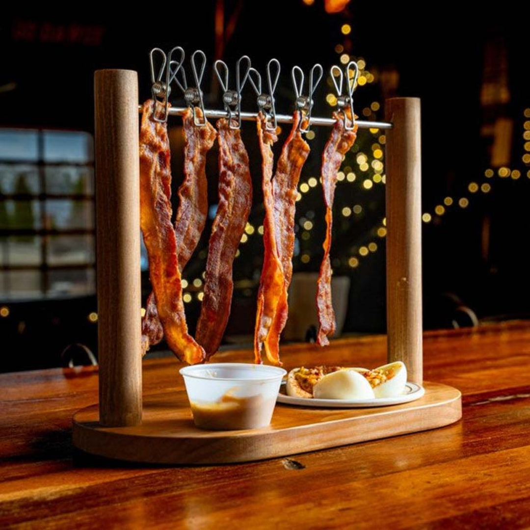 Wooden bacon rack with hanging bacon on a wooden table.