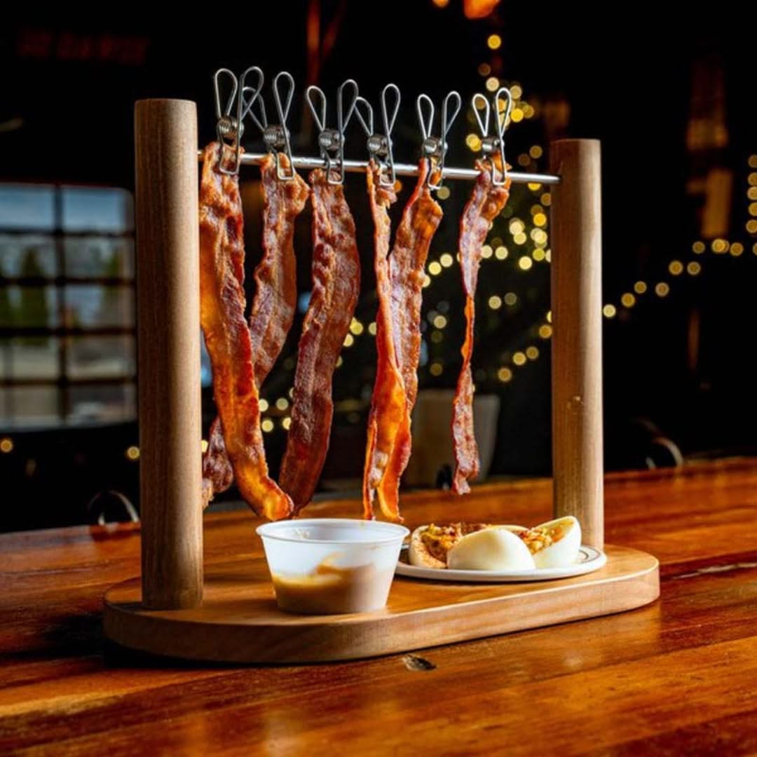 Wooden bacon rack with hanging bacon on a wooden table.