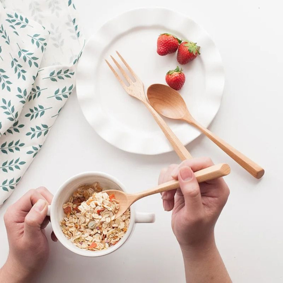 Person holding a wooden spoon over a bowl of cereal with strawberries on a plate in the background.