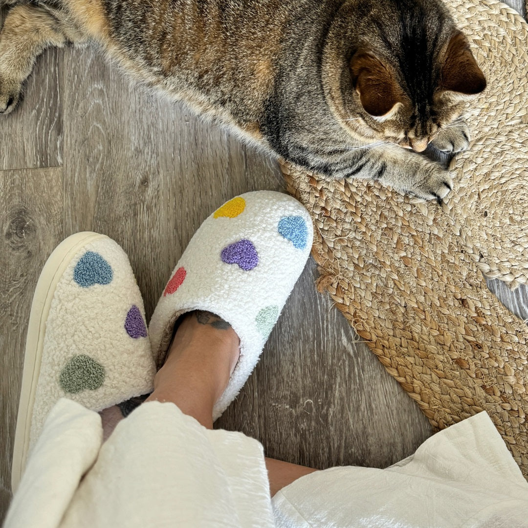 Person wearing colorful polka dot slippers on a wooden floor with a cat lying nearby.
