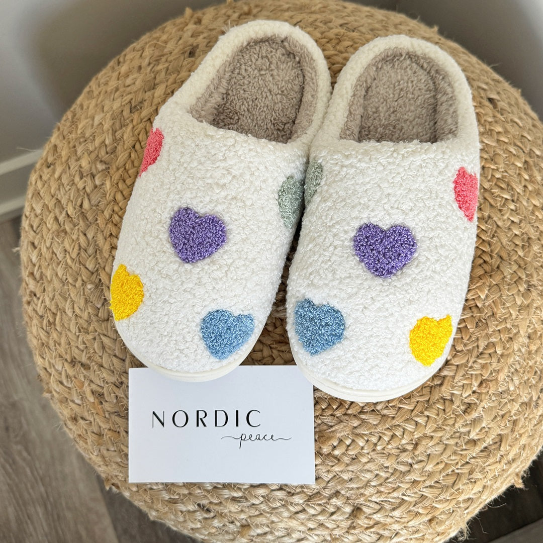 Pair of white slippers with colorful heart patterns on a woven mat, featuring the brand 'Nordic Peace'.