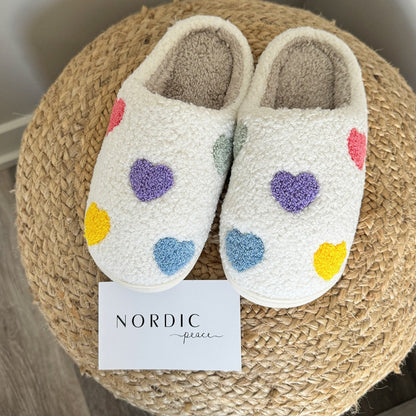 Pair of white slippers with colorful heart patterns on a woven mat, featuring the brand 'Nordic Peace'.