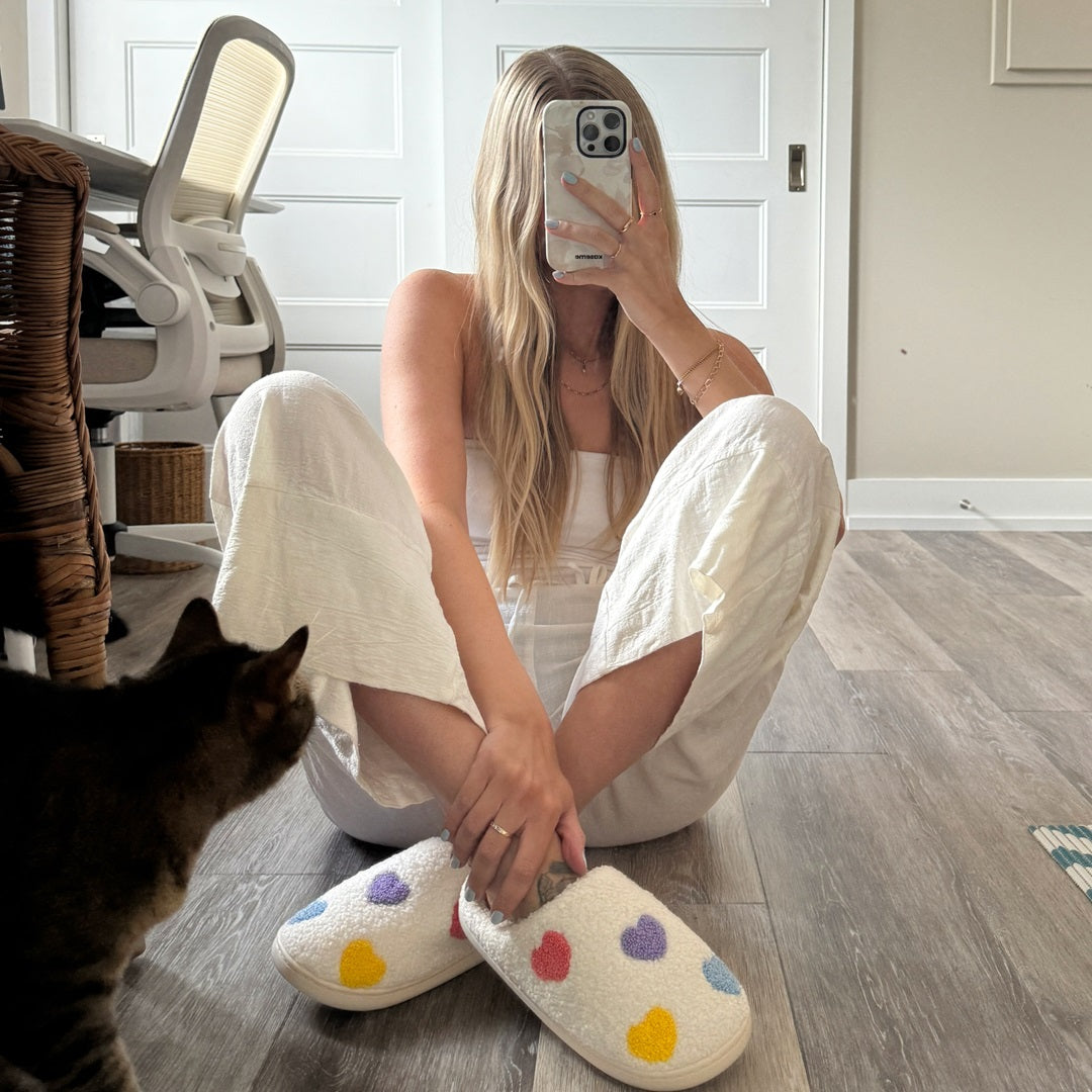 Woman sitting on the floor wearing colorful polka dot slippers, taking a mirror selfie.