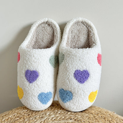 Pair of white slippers with colorful heart patterns on a woven surface.