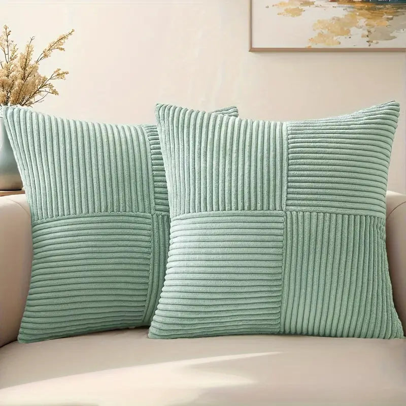 Two light green textured pillows on a beige sofa with a neutral wall and abstract painting in the background.